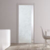 A modern room with white walls and light wood floors showcases an ECLISSE Pocket Door System—Classic Single Glass Doors 10mm (plain or patterned), plus a white table with a wire chair and a white cupboard holding tall vases and a plant.