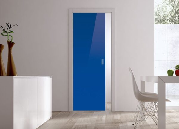 A modern, minimal room with light wood floors showcases a bright blue ECLISSE Pocket Door System (Classic Single Glass Doors 10mm). The space features white walls, a matching dining set, a sideboard, and two brown decorative vases.