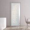 An ECLISSE Pocket Door Systems Classic Single Glass Door with frosted circles enhances a minimalist white room featuring a cupboard, dining table, white chair, decorative vases, and natural light from a window.