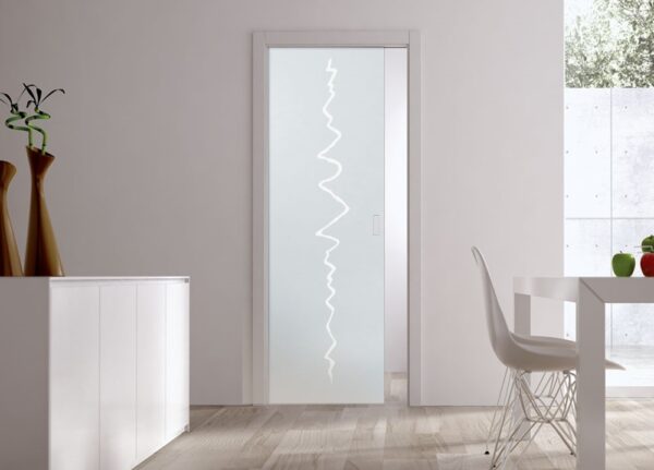 A modern interior with ECLISSE Pocket Door Systems - Classic Single Glass Doors featuring a frosted zigzag pattern, white walls, light wood floors, a sleek white cupboard with tall vases, and a dining table set by a large window.