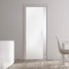 A minimalistic modern room featuring ECLISSE Pocket Door Systems - Classic Single Glass Doors (10mm, plain/patterned), white walls, light wood floor, a white cupboard with vases, and a white table with chairs by the window.