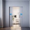 Modern hallway with ECLISSE Co-ordination Kit for Syntesis Flush Double Door System, opening to a bright room with a chair, framed artwork, plant, and chandelier. Blue arrows show the direction of door movement.