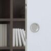 A close-up of a partially open ECLISSE Pocket Door featuring a Flush Pull Round Handle - Dia 57mm, with a blurred bookcase filled with books visible in the background.