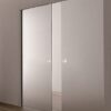 Two modern frosted glass pocket doors, featuring the ECLISSE Pocket Door System - Classic Double Plain Satin 8mm Glass with Stainless Steel Round Handles, are partially closed in a minimalist room with neutral walls and wooden floors.