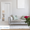 A bright living room with a light grey sofa, green cushions, and red roses on a white table. An open door with Rocket Door Frames - 75mm Fire Rated Pocket Door Kit displays the FD30 Approved fire safety logo and sleek pocket door design.