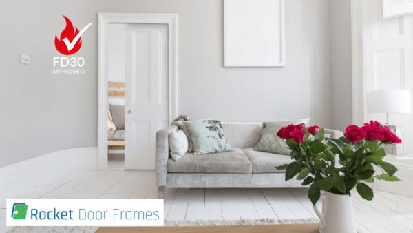 A bright living room with a light grey sofa, green cushions, and red roses on a white table. An open door with Rocket Door Frames - 75mm Fire Rated Pocket Door Kit displays the FD30 Approved fire safety logo and sleek pocket door design.