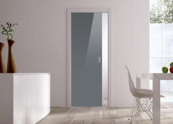 A modern interior features ECLISSE Pocket Door Systems - Classic Single Glass Doors (10mm), white walls, light wood floors, a white cupboard with vases on the left, and a dining table with white chairs by a large window.
