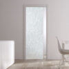 A modern interior with an ECLISSE Pocket Door Systems - Classic Single Glass Doors 10mm Plain or Patterned featuring a frosted leafy design, white walls, a sleek sideboard with tall vases, and a white dining table by a large window.