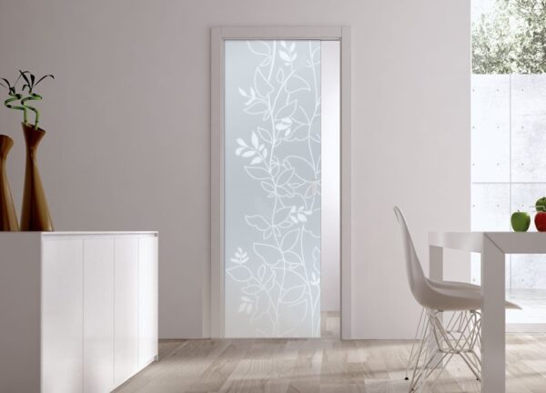 A modern, minimal living space features an ECLISSE Pocket Door System with a 10mm patterned glass door, white furniture, and wooden flooring. Sunlight streams in from a large right-side window.