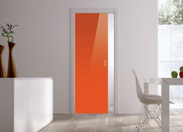 A modern interior features ECLISSE Pocket Door Systems – Classic Single Glass Doors 10mm, bright orange in colour, white walls, a cupboard with vases to the left, and a dining table with chairs to the right. Natural light highlights the stylish glass sliding doors.