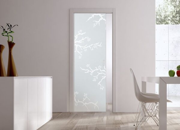 A modern room with light wood floors, a white sideboard, two brown vases, a white table and chair, and an ECLISSE Pocket Door Systems - Classic Single Glass Doors 10mm Plain or Patterned leading to a bright outdoor space.