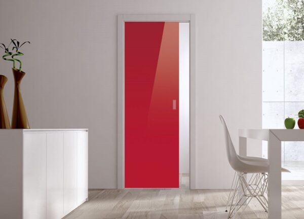 A modern interior with an ECLISSE Pocket Door Systems Classic Single Glass Door (10mm plain) in glossy red set in a white wall, light wooden floor, a white cabinet with vases on the left, and part of a white dining table and chair on the right.