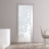 A modern interior with an ECLISSE Pocket Door Systems - Classic Single Glass Doors 10mm Plain or Patterned featuring a white bubble pattern, white furniture, tall vases with plants, and a window overlooking a concrete wall and greenery.