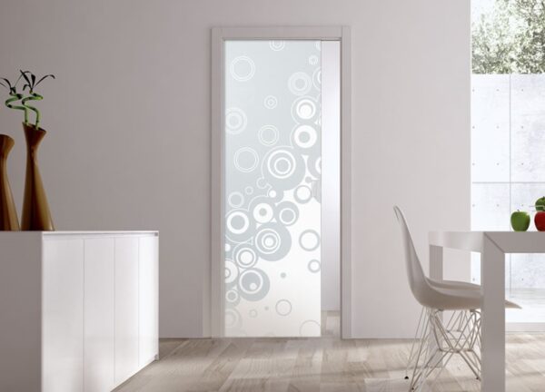 A modern interior with an ECLISSE Pocket Door Systems - Classic Single Glass Doors 10mm Plain or Patterned featuring a white bubble pattern, white furniture, tall vases with plants, and a window overlooking a concrete wall and greenery.