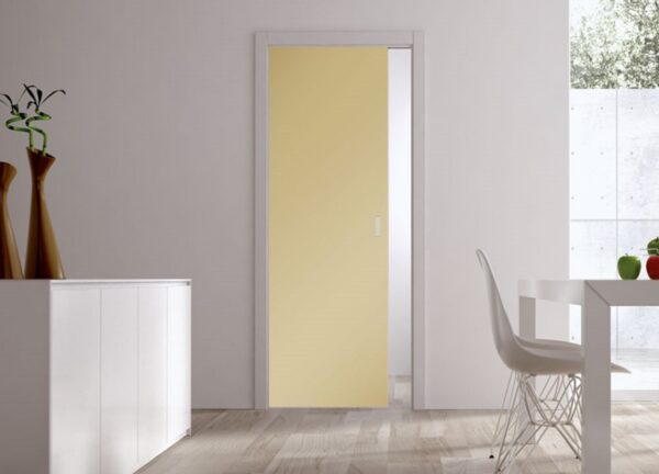 A modern, minimalistic room featuring the ECLISSE Pocket Door Systems - Classic Single Coloured Glass Door 10mm in light yellow, white walls, a white cabinet with vases, a white dining table and chair by a large window.
