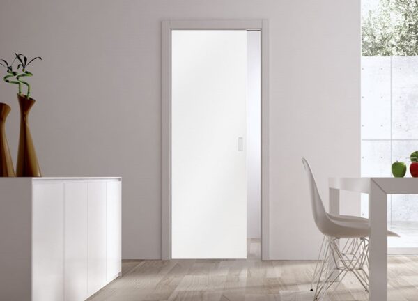 Minimalist room featuring white walls, a modern sideboard with vases, a white dining table and chair, and an ECLISSE Pocket Door Systems - Classic Single Glass Doors 10mm (plain or patterned). Natural light shines through the window on the right.