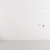 Minimalist interior with a plain white wall and a Rocket Door Frames - ULTRA Flush Hinged door on the right. On the left, three black vases with thin branches and red berries sit on the glossy floor, creating a simple, uncluttered scene.