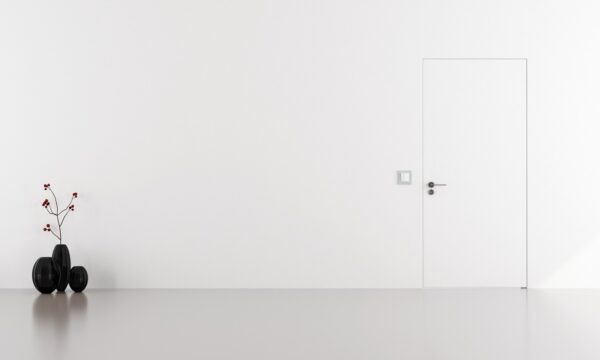 Minimalist interior with a plain white wall and a Rocket Door Frames - ULTRA Flush Hinged door on the right. On the left, three black vases with thin branches and red berries sit on the glossy floor, creating a simple, uncluttered scene.