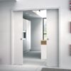 A modern white kitchen with sleek cupboards and appliances is visible through open ECLISSE Classic Double Pocket Door Kit doors; large windows fill the space with natural light.