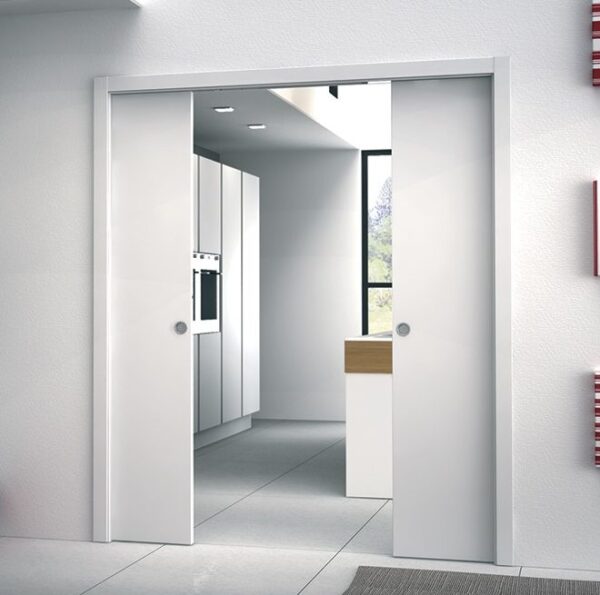 A modern white kitchen with sleek cupboards and appliances is visible through open ECLISSE Classic Double Pocket Door Kit doors; large windows fill the space with natural light.
