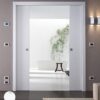 An ECLISSE Pocket Door System - Classic Double Wiring-Ready leads to a minimalist bathroom with a white bath, wooden stool, and green vine on the wall. Modern lighting and control panels complete the sleek, refined look.