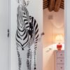A white ECLISSE Door system - Syntesis® Hinged Single With Door, featuring a black and white zebra illustration, is partially open to a small room with a red lamp on a white chest of drawers and exposed wooden ceiling beams.