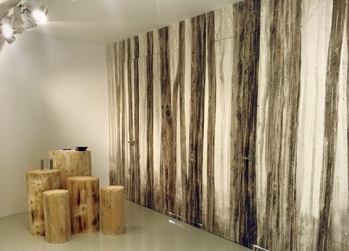 A modern room with a black and white forest mural, tree trunk stools and table, complemented by the seamless ECLISSE Door system - Syntesis® Hinged Single With Door for a sleek, woodland-inspired décor.