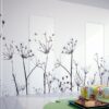Minimalist room with white walls, a black botanical mural, and modern decor. The ECLISSE Door system - Syntesis® Hinged Single With Door blends seamlessly into the space. Colourful cushions and a glass coffee table complete the look; sunlight streams in through a large window.
