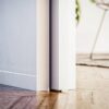 Close-up of the ECLISSE Pocket Door System - Syntesis® Single Wiring-Ready slightly open, sunlight casting shadows on a wooden floor. A blurred chair and plant in the background highlight the bright, modern interior.