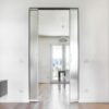 A modern, bright room features the ECLISSE Pocket Door System - Syntesis® Double Wiring-Ready, opening to a dining area with a table, chairs, pendant light, and large windows that fill the space with natural light.