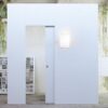 A minimalist white wall with the ECLISSE Pocket Door System - Syntesis® Single Wiring-Ready and a glowing wall light stands in an industrial space, featuring green mould on the back wall and large numbered grids on the left.