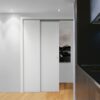 A modern interior with white ECLISSE pocket doors partially open, revealing black-and-white wall art. The light wood floor and a section of dark kitchen worktop add contrast, whilst recessed ceiling lights provide illumination.