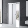 A modern interior with large windows and city views features an ECLISSE Pocket Door System - Telescopic Sliding Single set in a dark wall with city line art. Minimalist white shelves are mounted on the right.