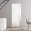 A modern minimal room features the ECLISSE Syntesis® Flush (No Architrave) 10mm Glass Pocket Door System Coloured, complemented by a white sideboard, table, chair, and a fruit bowl. A diagonal label reads “No Architrave.”.