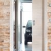 A black compact car is parked in a bright garage, visible through a partially open ECLISSE Pocket Door System - Classic Single Wiring-Ready set in a stone-patterned wall with light switches and a thermostat on the right.