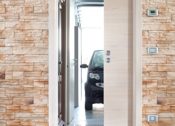 A black compact car is parked in a bright garage, visible through a partially open ECLISSE Pocket Door System - Classic Single Wiring-Ready set in a stone-patterned wall with light switches and a thermostat on the right.