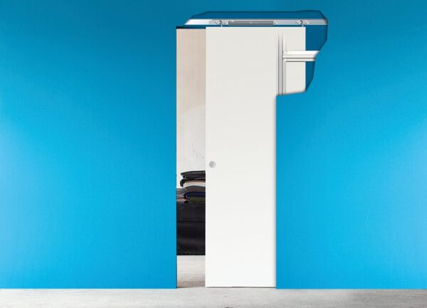 A white pocket door with an exposed ECLISSE Bias Soft Closer for Pocket Doors (Single) track is partially open against a bright blue wall, revealing a small stack of folded clothes in the adjoining room.
