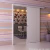 A modern room with pastel striped wallpaper and a white ECLISSE Wall Mounted Sliding Door Kit-2m Track-Paris 1, a purple vase with twigs, and a dining area beyond. Text reads: “Pelmet and doorpost not included with Paris 1.”.