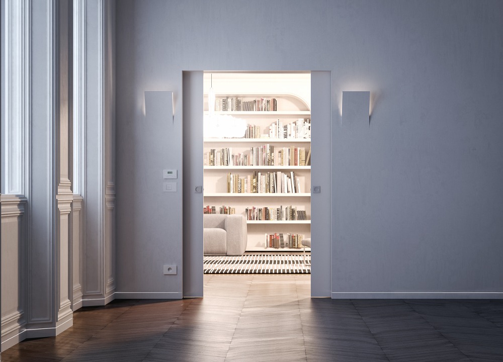 A doorway with white walls opens to a bright room featuring tall bookcases filled with books, a cosy chair, and a striped rug. Sunlight filters in through large windows on the left, while sleek pocket doors maximise space and style.