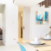 A modern dining area with a light wood table for two, an abstract painting, and a partially open cavity slider pocket door frame kit leading to the hallway. Neutral tones and clean lines give the space a minimalist feel.