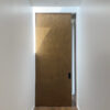 A narrow corridor with white walls and a wooden floor leads to a large sliding door fitted with the Cavity Slider Pocket Door Frame Kit, its minimalist, modern design partially illuminated by sunlight from above.